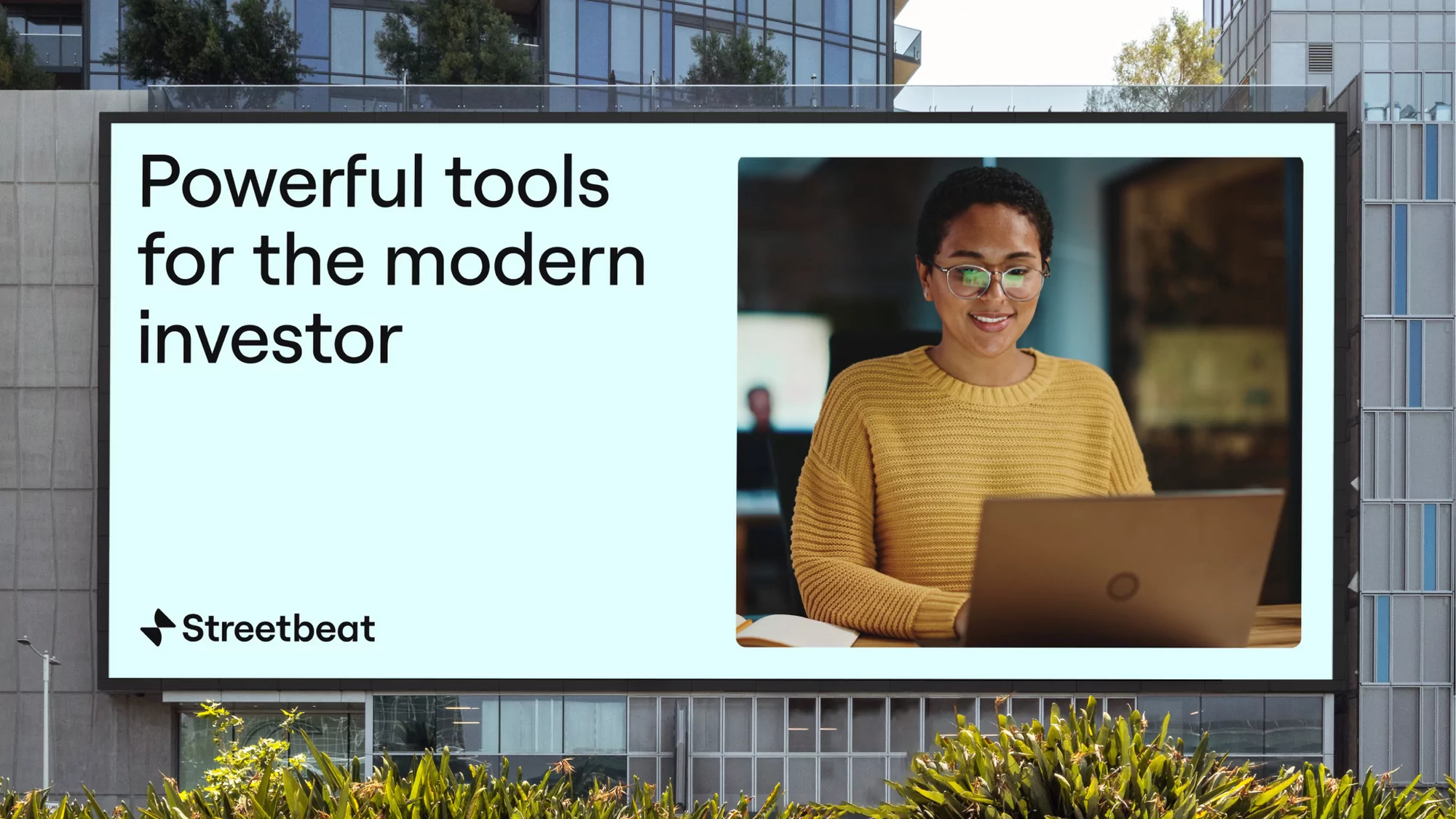 Digital billboard for Streetbeat showing a woman in a yellow sweater using a laptop alongside text reading Powerful tools for the modern investor