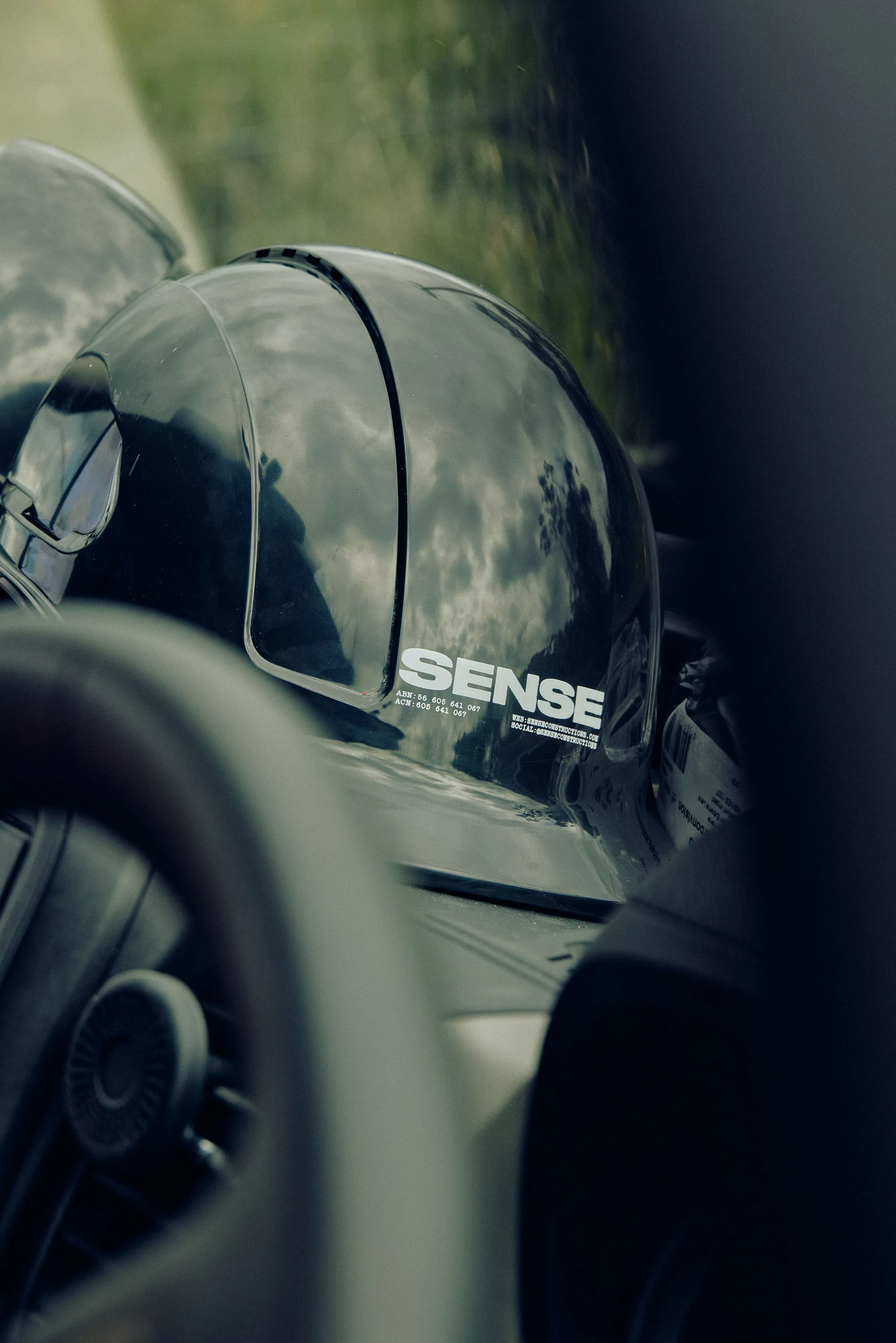 Close-up of a glossy black helmet with 'SENSE' logo inside a vehicle, featuring car interior elements like steering wheel and dashboard.
