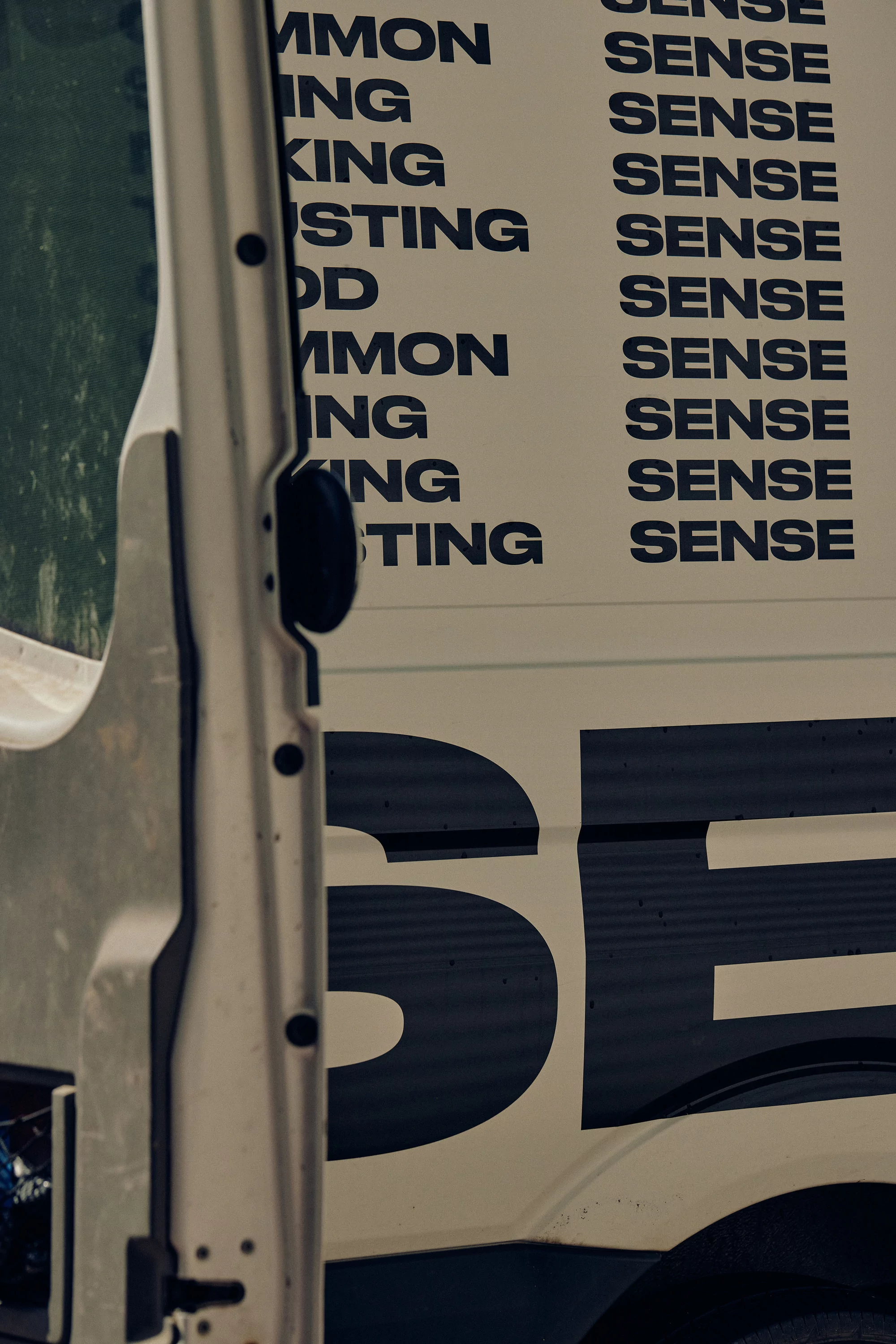 Close-up of the side of a van with large block letters spelling 'Sense' and other partial words, creating an abstract text pattern.