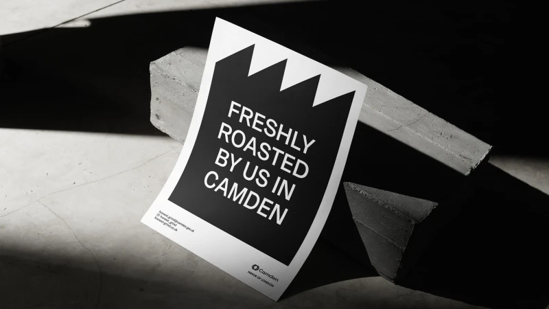 Promotional poster for freshly roasted coffee by Camden, resting against concrete blocks in a studio with bright, graphic lighting.
