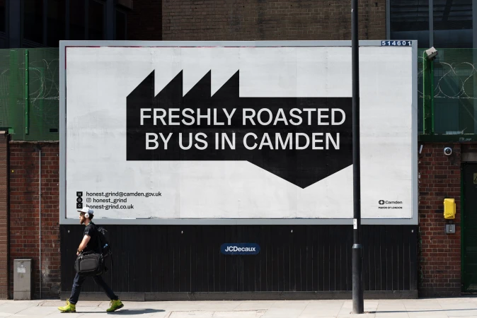 Man walks by a large billboard advertising freshly roasted coffee in Camden, featuring bold black text and graphic elements on white.