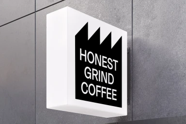 Honest Grind Coffee brand identity sign mounted on a textured grey concrete wall exterior.