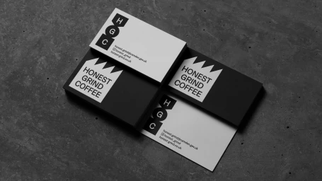 Stacks of black and white business cards featuring Honest Grind Coffee branding on a dark concrete background.