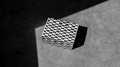 Black and white patterned product packaging box resting on a grey concrete surface under stark directional lighting.