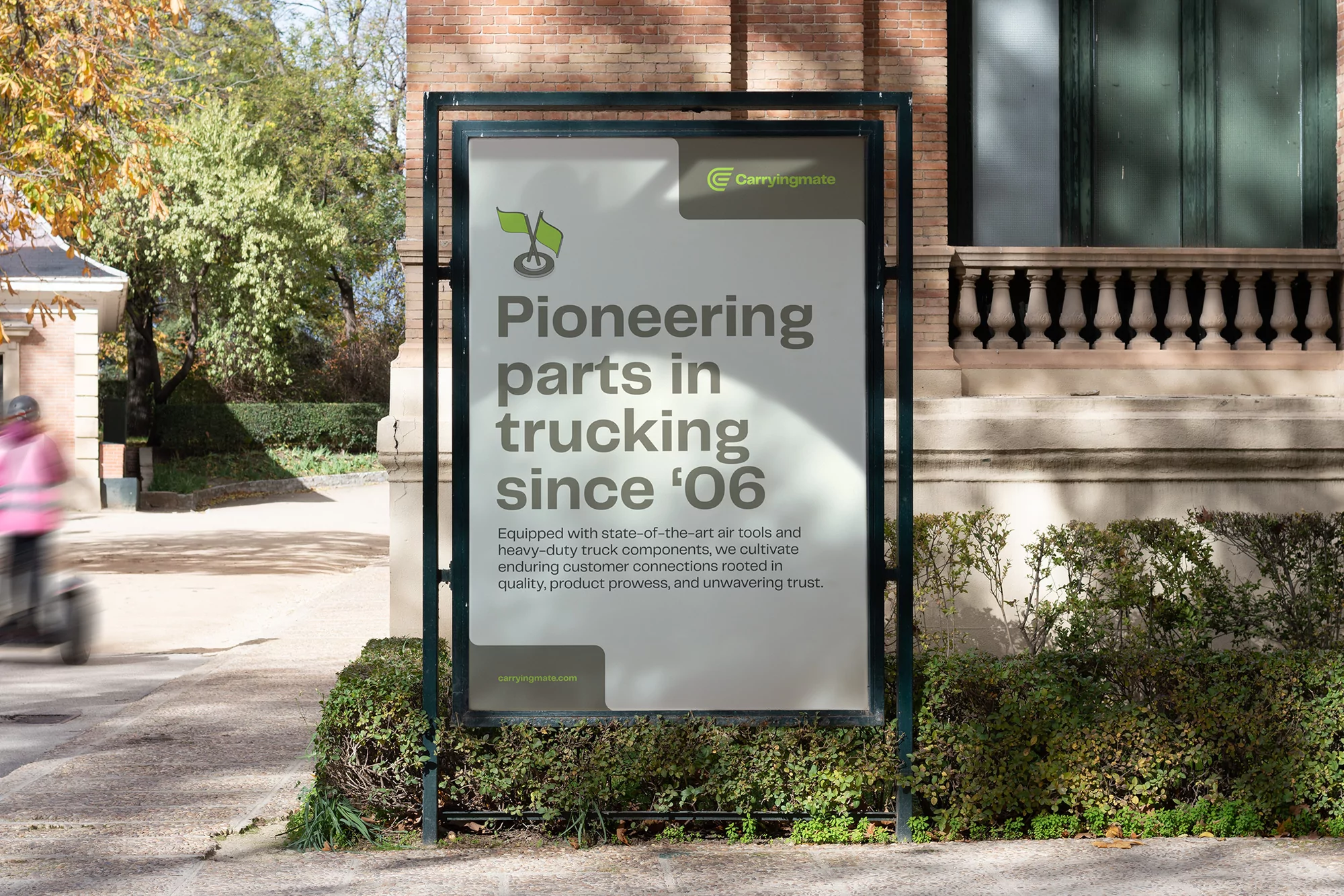 Outdoor advertisement for Carryingmate trucking parts, displayed on a modern billboard surrounded by greenery in an urban setting.