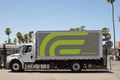 Side view of a white delivery truck branded with Carryingmate logo parked on a street with palm trees.