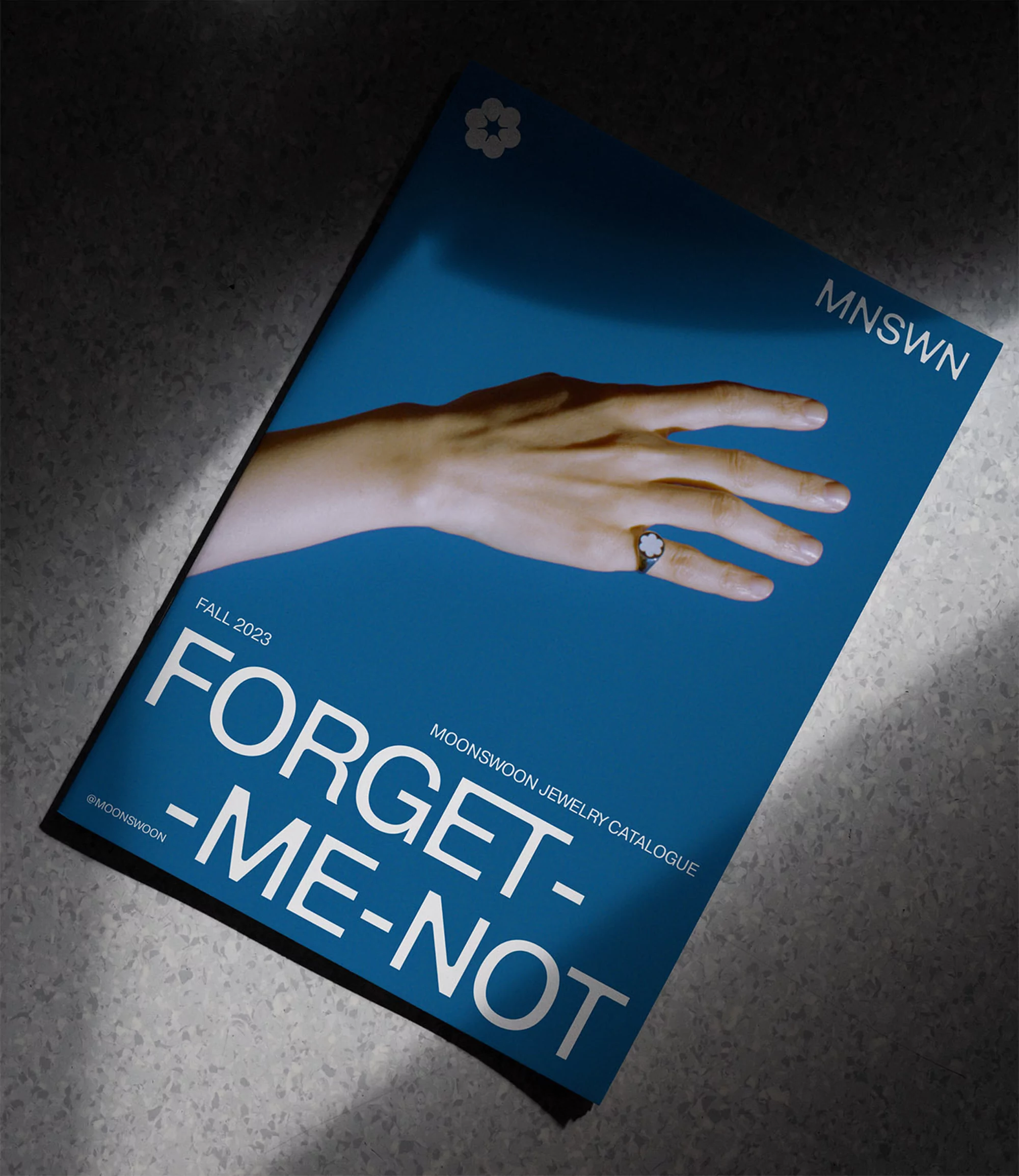 Jewelry catalogue cover featuring an open hand wearing a ring against a blue background, shadowed texture, and product branding.