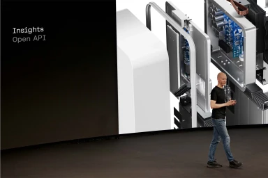 Man walking on a dark stage in front of a large screen displaying a 3D cutaway diagram of a device