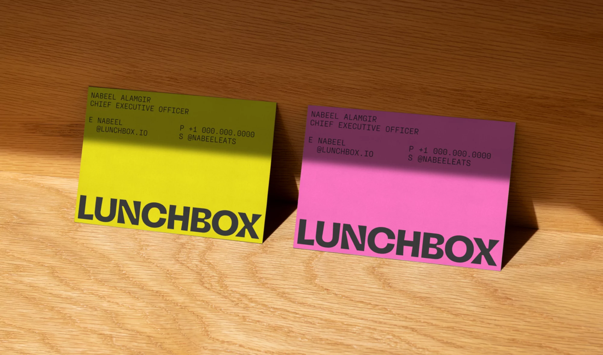 Two brightly colored business cards, one yellow and one pink, rest on a wooden surface in soft, natural light, showcasing minimal design.