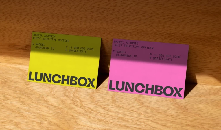 Two brightly colored business cards, one yellow and one pink, rest on a wooden surface in soft, natural light, showcasing minimal design.