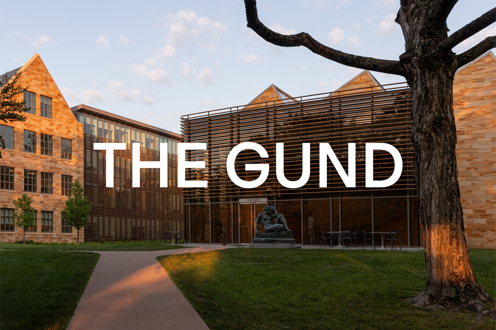 Exterior view of The Gund building featuring modern architecture, stone facade, lawn, pathway, and a sculpture.