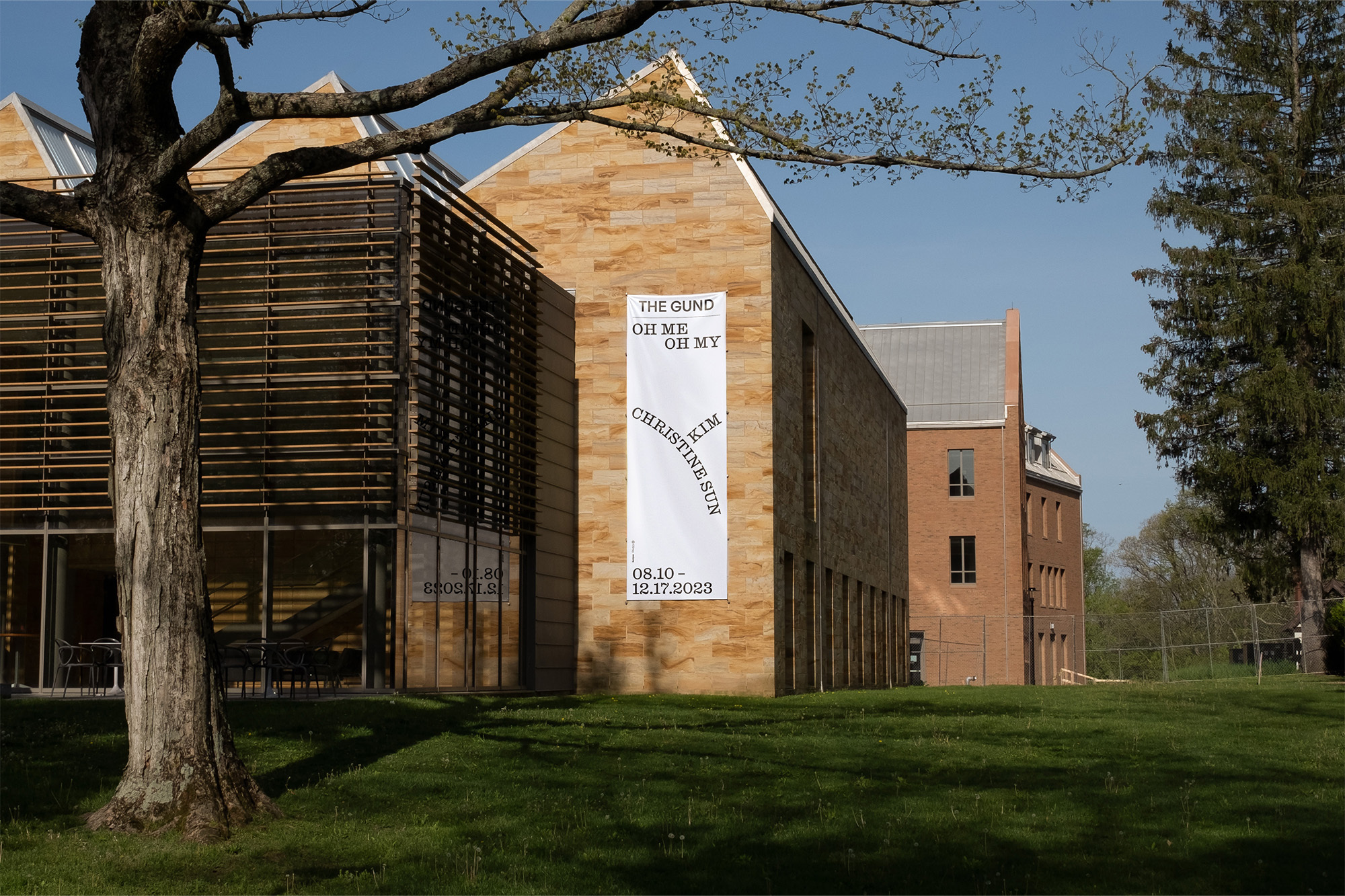 Exterior shot of a contemporary building with a banner for Christine Sun Kim's exhibition, 'The Gund Oh Me Oh My', on a green lawn.