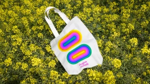 White canvas tote bag with a colourful concentric oval graphic resting among yellow wildflowers.