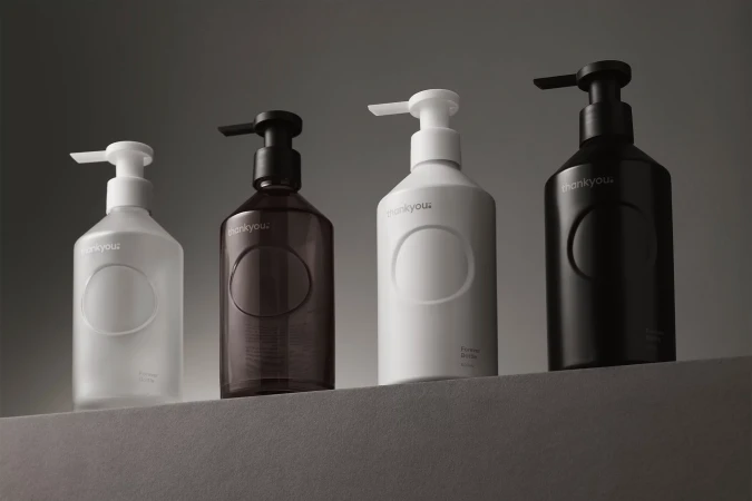 Four Thankyou Forever Bottles in white, brown, and black colors with pump dispensers, arranged on a neutral gray surface against a gray background.