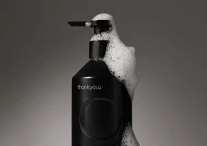 Black soap dispenser bottle with white foam covering the pump and upper shoulder against a grey background.