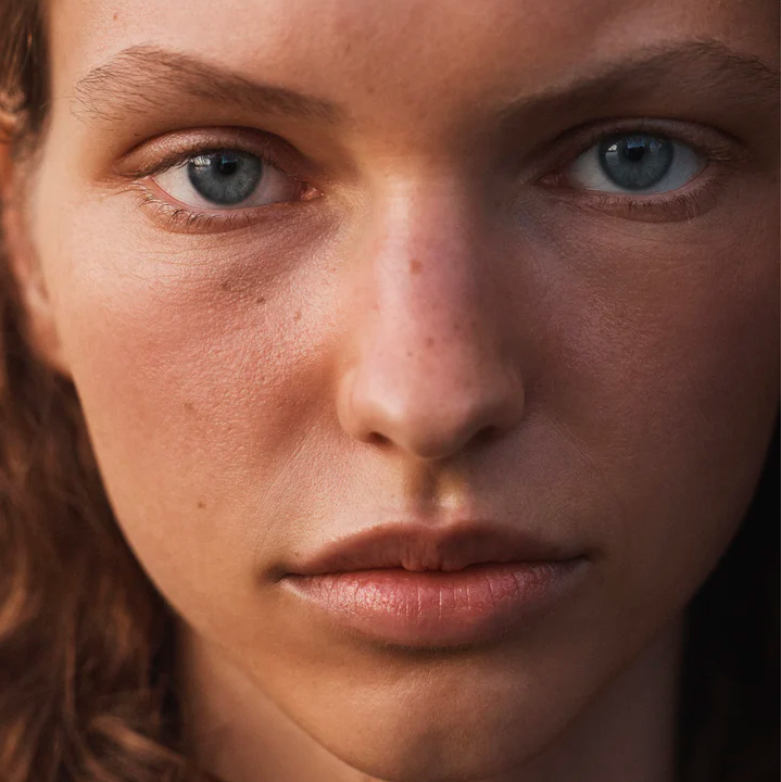 Close-up portrait of an adult female with fair skin, striking blue eyes, and light brown hair, looking directly at the camera with a neutral expression.