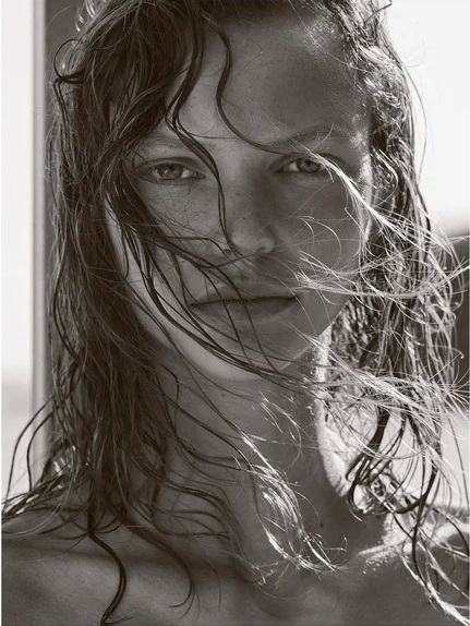 Close-up portrait of a woman with wet hair partially covering her face, captured in black and white with natural light.