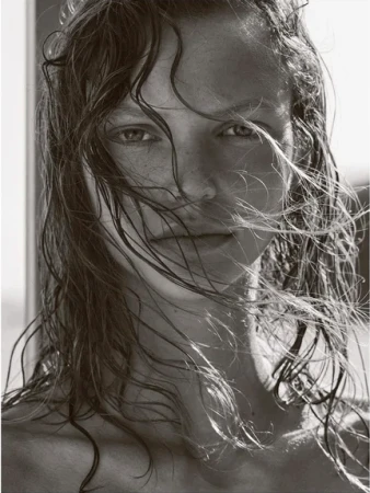 Close-up portrait of a woman with wet hair partially covering her face, captured in black and white with natural light.