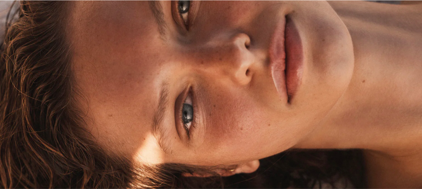 Close-up shot of a young adult woman with light skin, brown hair, and blue eyes looking at the camera with a calm facial expression.