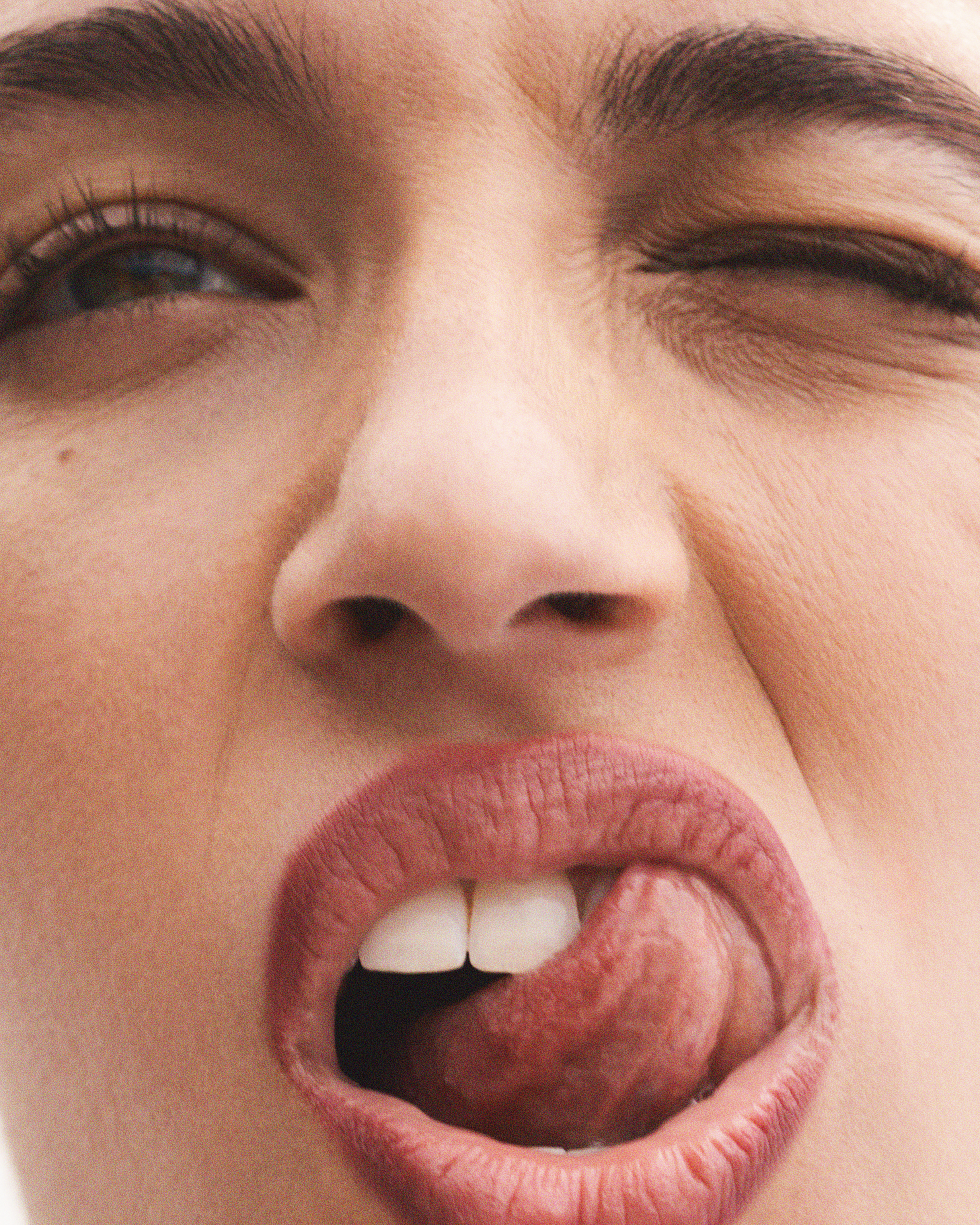 Close-up of a woman with tan skin sticking out her tongue. The woman winks one eye closed for a playful and emotive portrait.