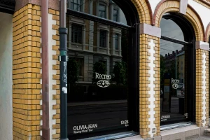 Storefront windows with yellow brick columns displaying Recreo branding and tour dates for Olivia Jean in black glass