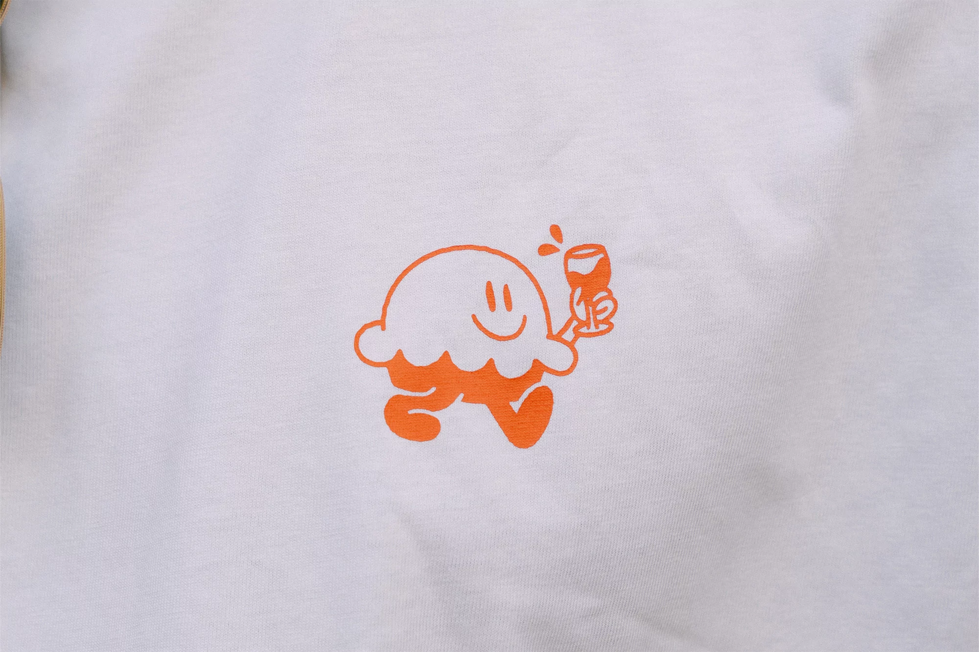 A white t-shirt features an orange cartoon graphic of a smiling figure holding a wine glass, adding a playful and whimsical touch.