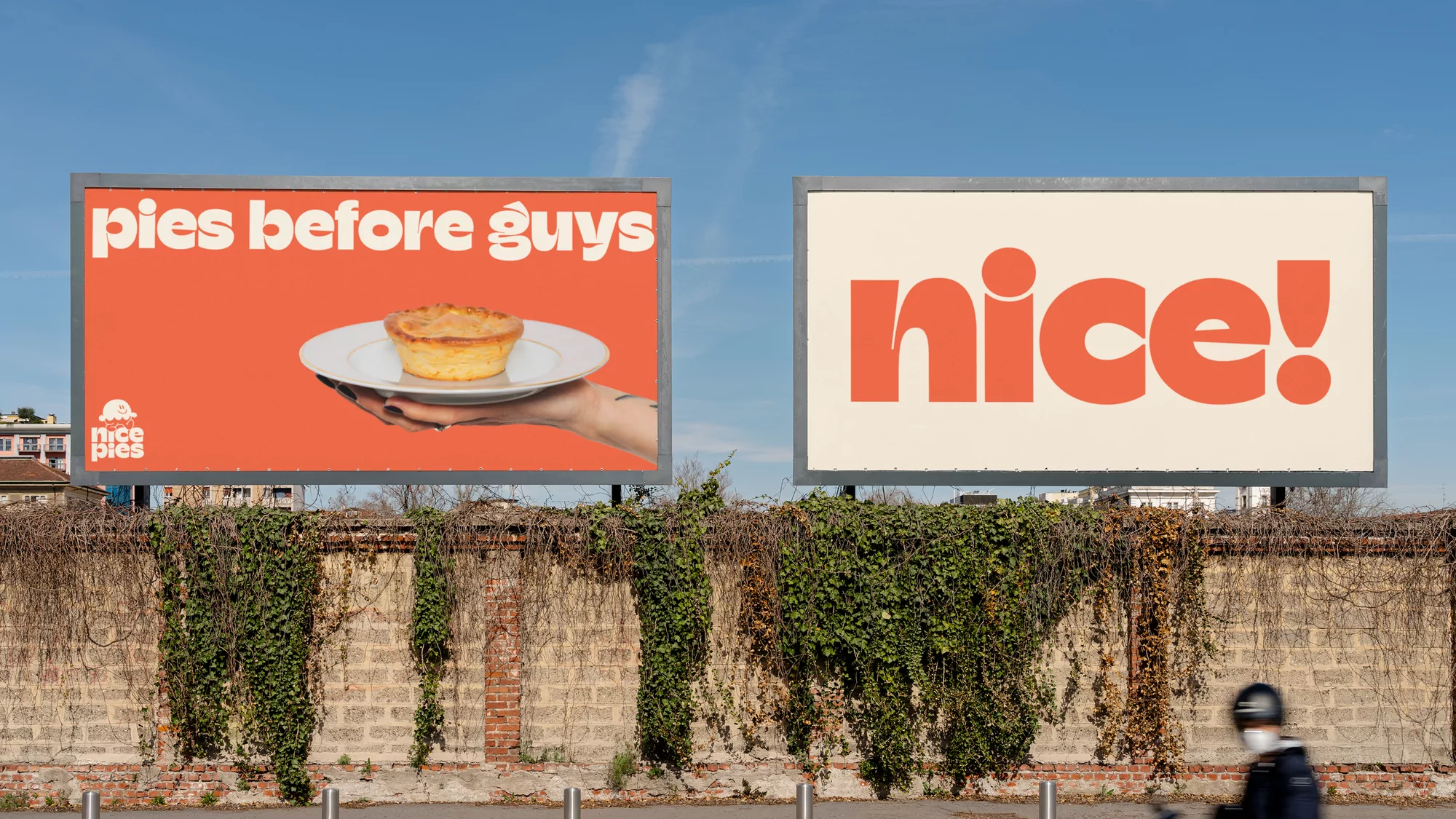 Two billboards display food ads: one showcases a pie held by a hand, while the other simply reads 'nice!', set against a clear blue sky.