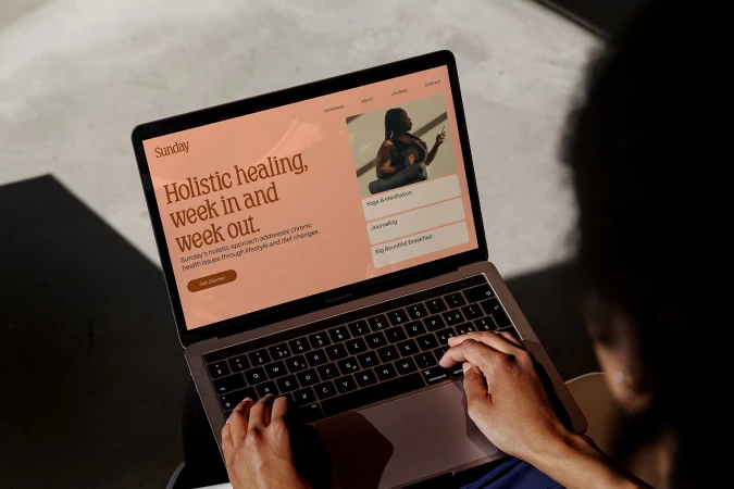 Person using a laptop to view a website with holistic wellness content; website features text, an image of a woman, and navigation buttons.