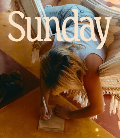 Woman relaxes in hammock, writing in a notebook on a sunny day. Indoor leisure scene with muted tones.