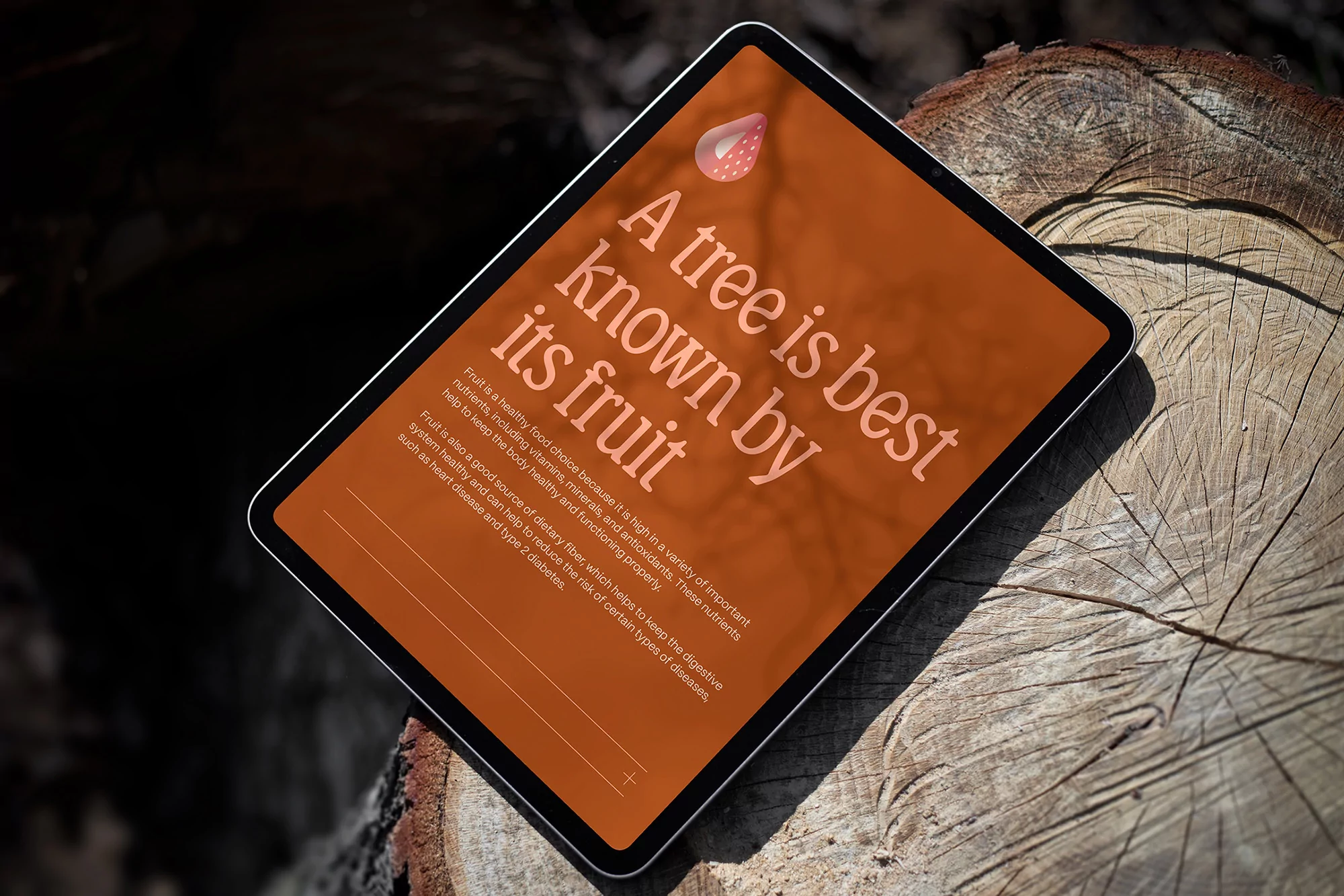 Tablet displays the text: A tree is best known by its fruit; with a strawberry graphic, against a wooden log background.