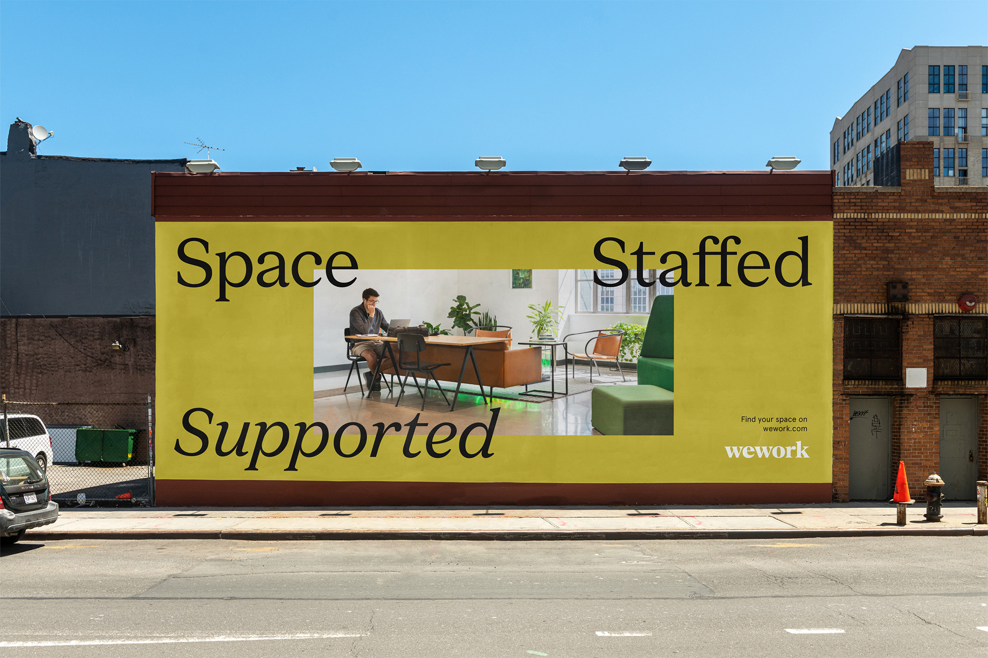 Exterior view of a WeWork advertisement painted on a building, showing a man working in a modern office space with a laptop.