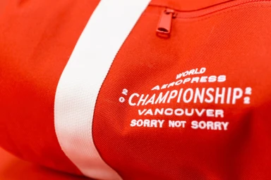 Close-up detail of a bright red fabric bag with a vertical white stripe and printed white text for World Aeropress Championships.