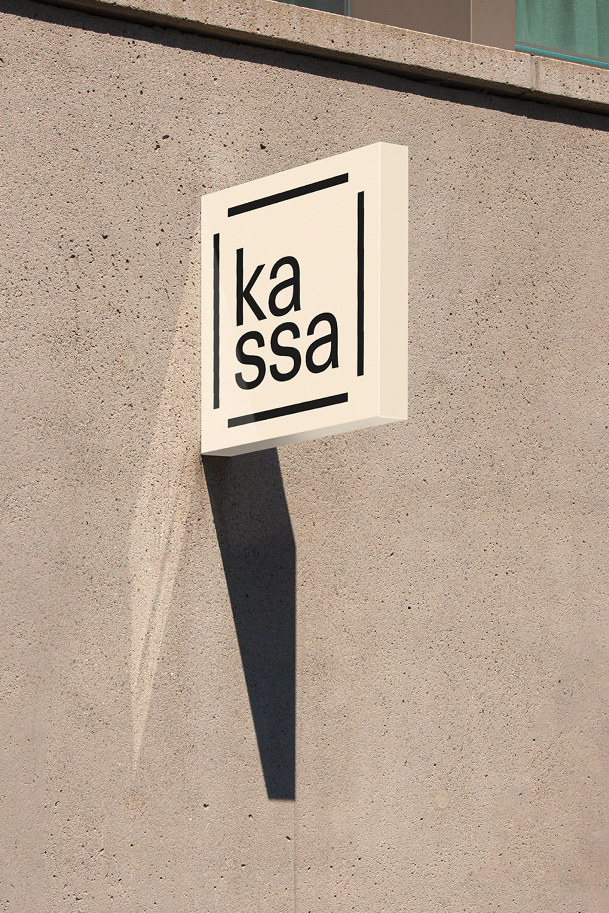 Illuminated sign on a textured wall displaying the text 'kassa' in a black, sans-serif font, creating a modern, minimalist aesthetic.