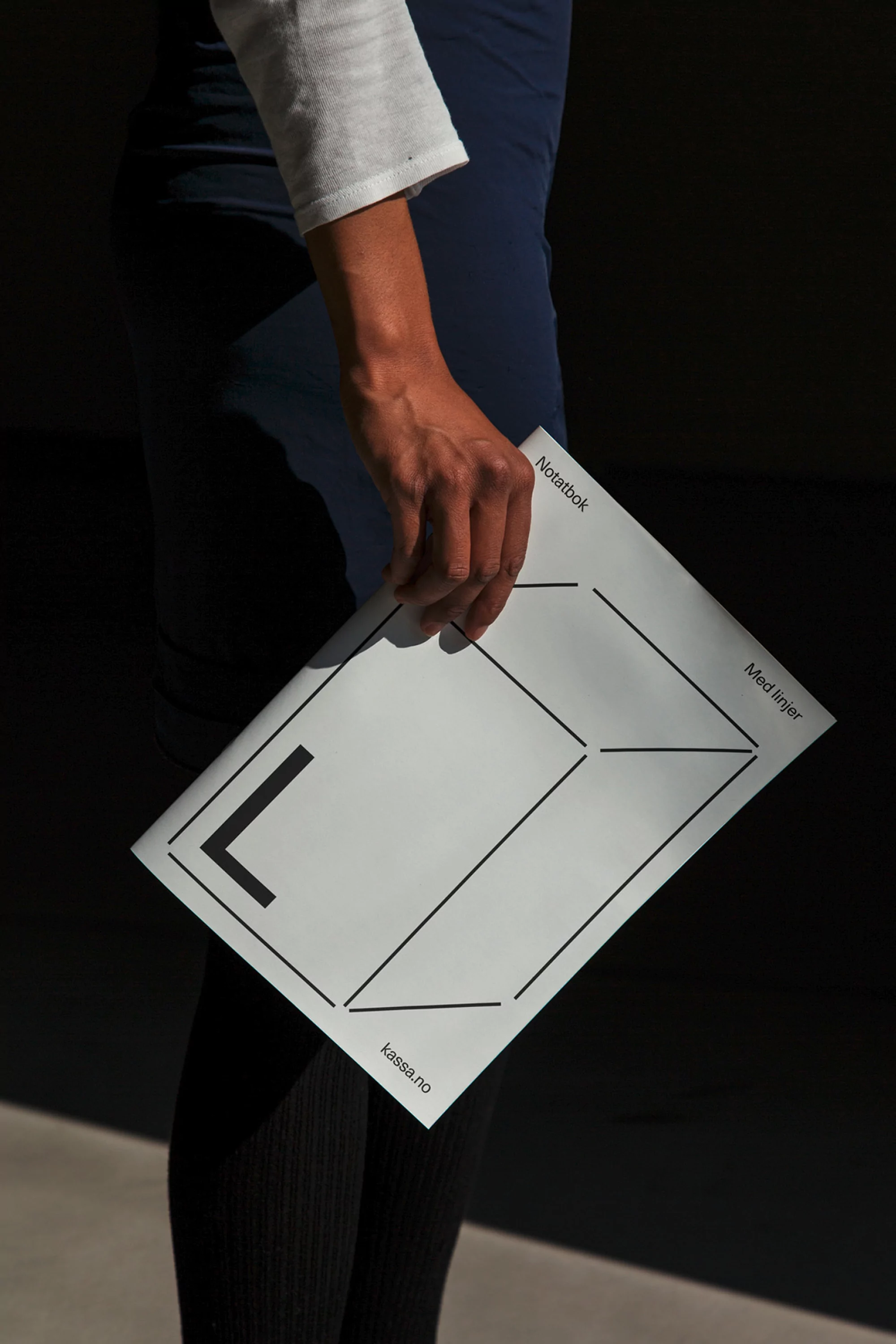 Close-up of a person holding a branded paper notebook with geometric line art against a dark background