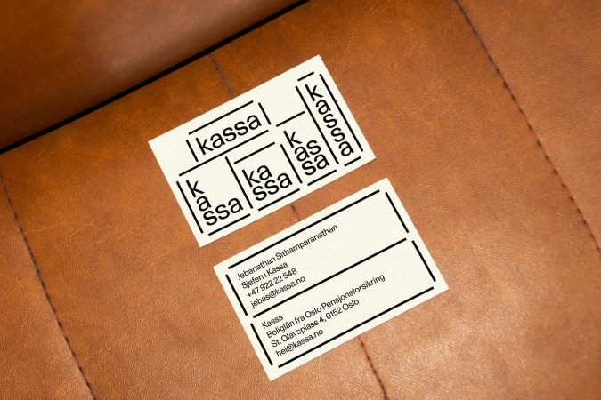 Two 'kassa' business cards on brown leather surface. One card features logo variations; other lists contact info with Oslo address.