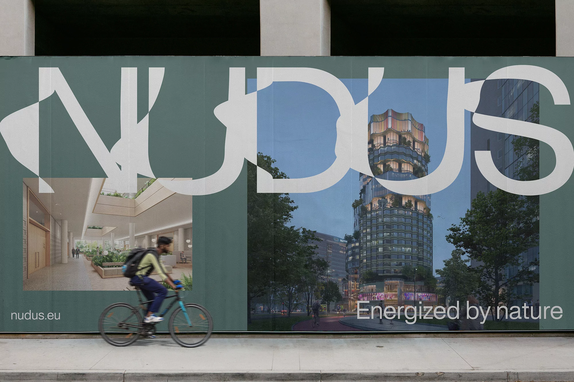Man riding a bicycle past a construction hoarding featuring NUDUS branding and architectural renderings of building interiors and exteriors.