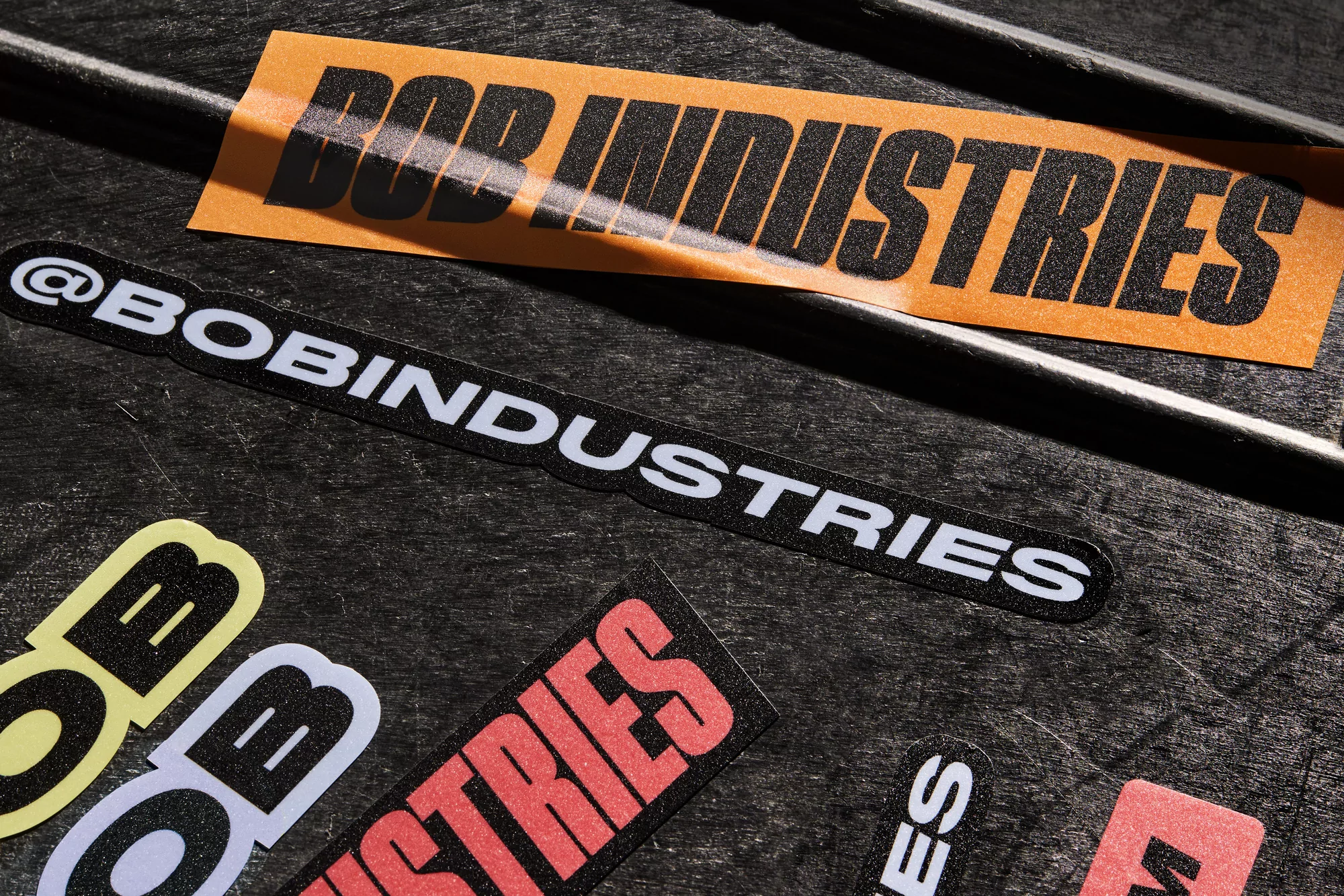 Close-up of an arrangement of colorful logo stickers that read 'BOB INDUSTRIES' in black and white on a dark gray background.