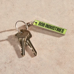 A metal keychain with two brass keys and a lime green branded tag resting on a textured beige surface.