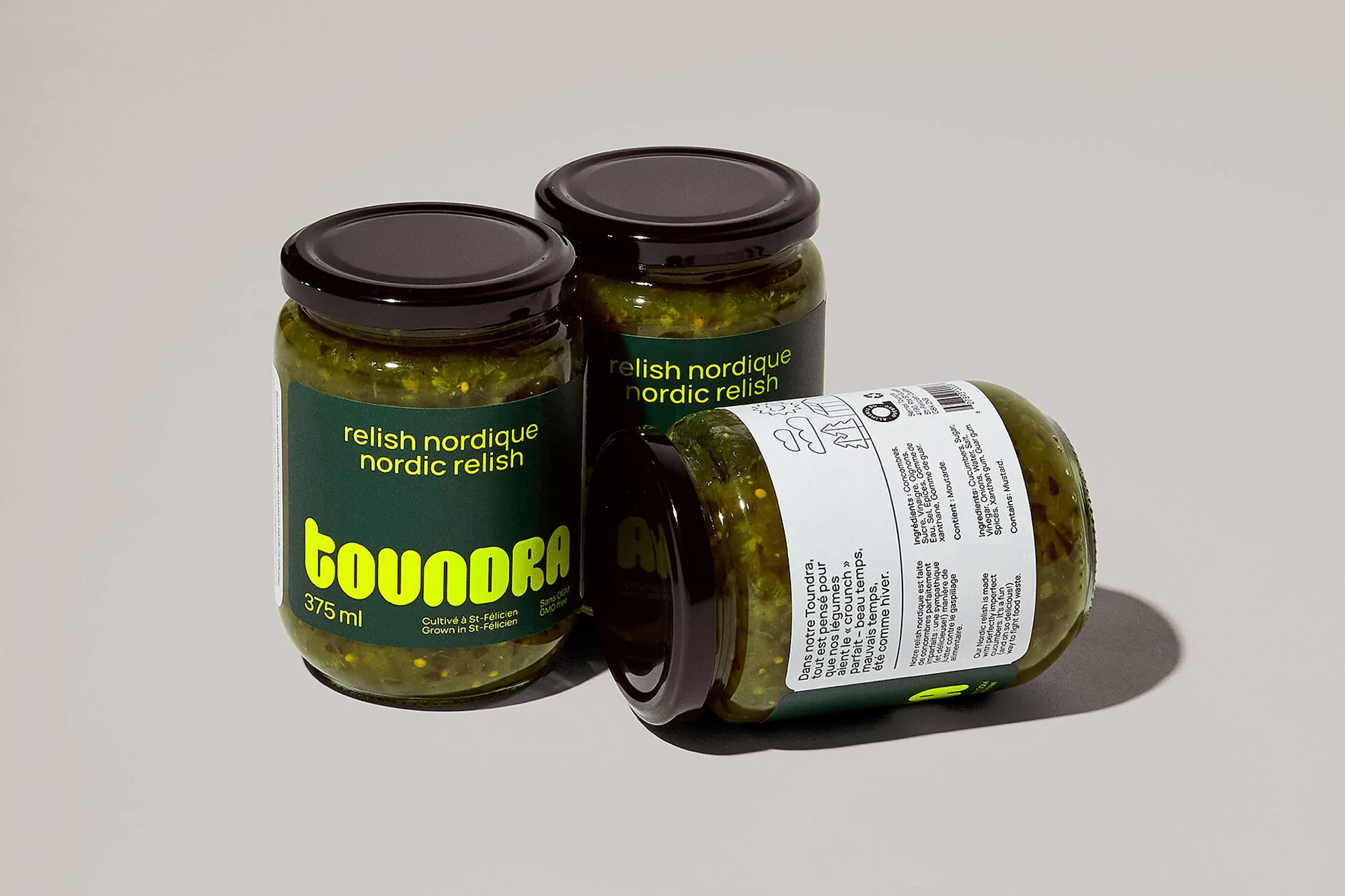 Three jars of Toundra Nordic Relish sit on a gray surface, two standing upright and one laying horizontally, all with black lids.