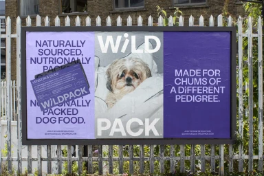 Outdoor advertising billboard for Wild Pack dog food featuring purple posters with bold typography and a dog resting on pillows