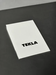White branded booklet featuring bold black typography resting on a dark textured surface