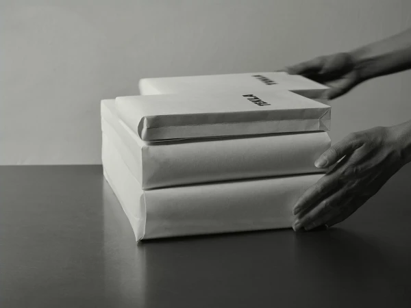 Monochrome image of hands arranging wrapped paper packages marked with brand text on a dark surface.