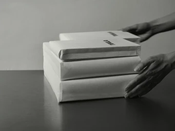 Monochrome image of hands arranging wrapped paper packages marked with brand text on a dark surface.
