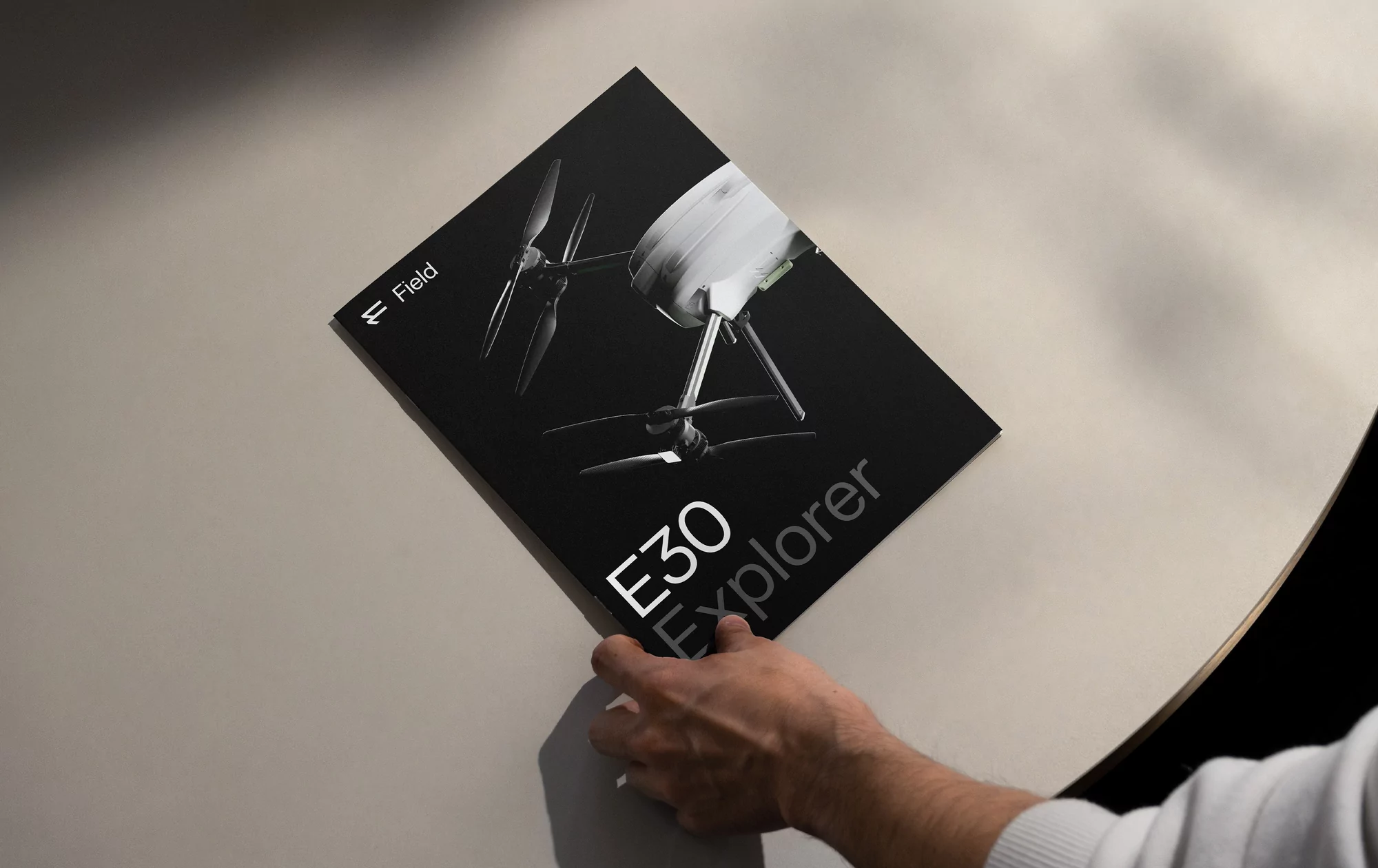 Promotional image featuring a black booklet on a beige surface, spotlighting the 'E30 Explorer' drone model and minimal design elements.