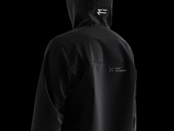 Back view of a person wearing a black hooded jacket with white graphic branding against a black background.