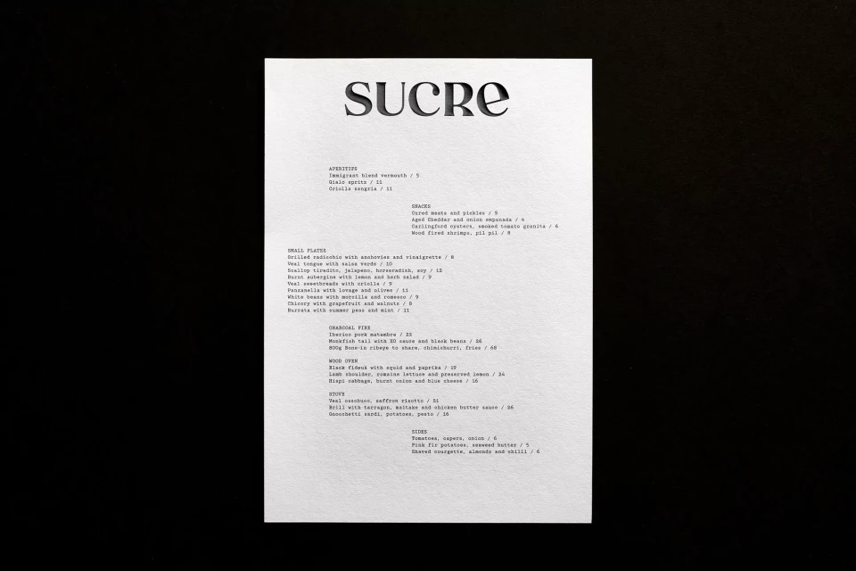 Sucre restaurant menu on a white paper featuring appetizers, small plates, charcoal fire, wood oven, sides, and stews.