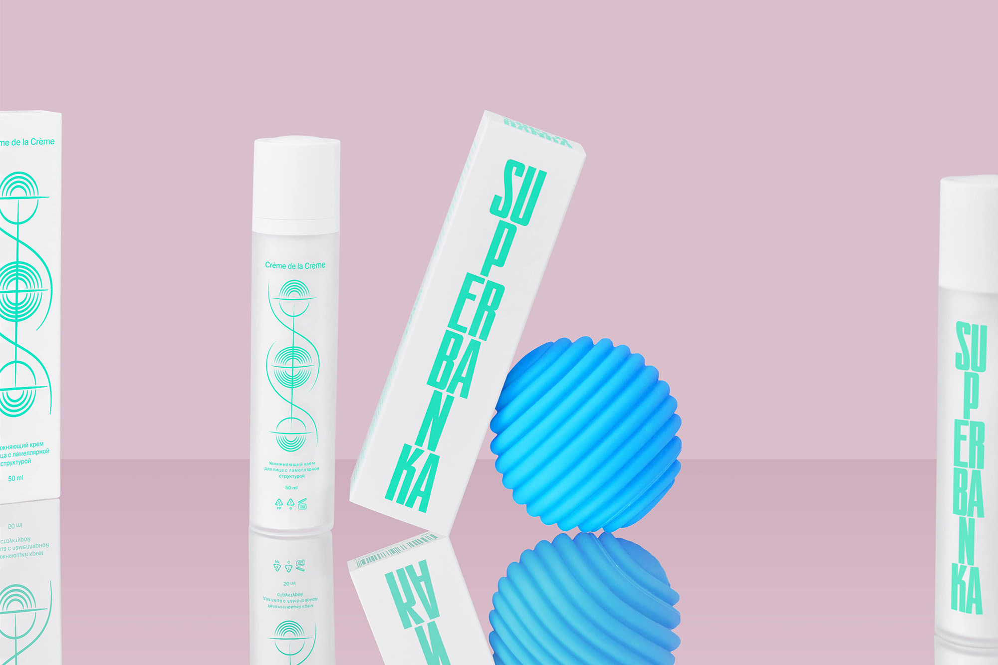 Product shot of white and teal skincare containers and a blue sphere on a reflective surface against a pale pink background.