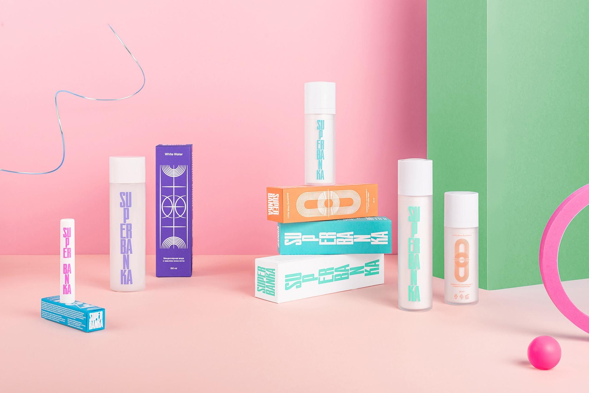Still life product shot of Super Baka skincare line featuring cleanser bottles and product boxes against a split pink and green backdrop.