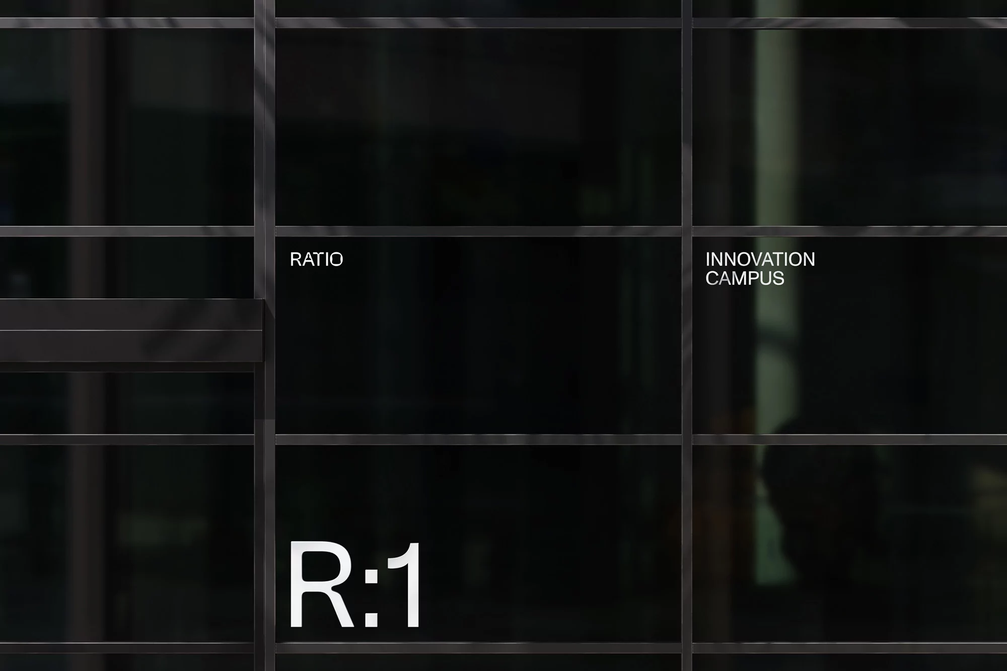 Architectural shot of a dark building facade with metal grid, reflecting 'Innovation Campus' and company identity 'R:1' and 'Ratio'.