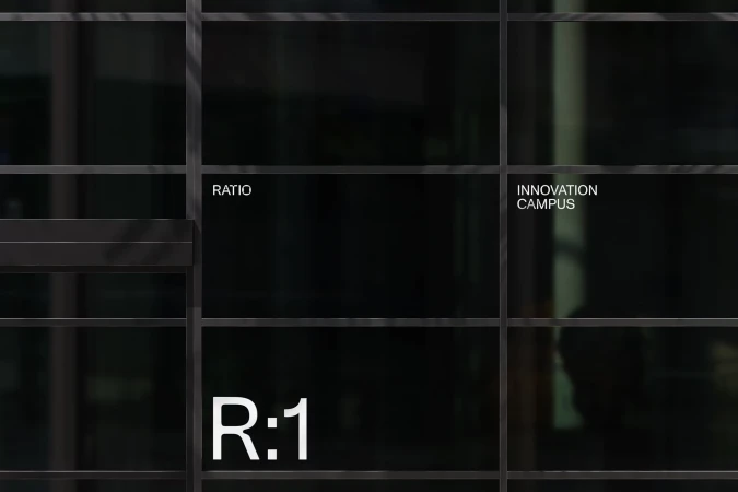 Architectural shot of a dark building facade with metal grid, reflecting 'Innovation Campus' and company identity 'R:1' and 'Ratio'.
